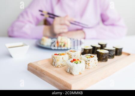 Panini di sushi su piatto di legno davanti alla donna usando i chopsticks, concetto giapponese di pasto. Foto Stock