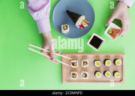 Vista ad alto angolo delle donne che tengono i bastoncini per raccogliere il sushi roll dal piatto al ristorante. Foto Stock