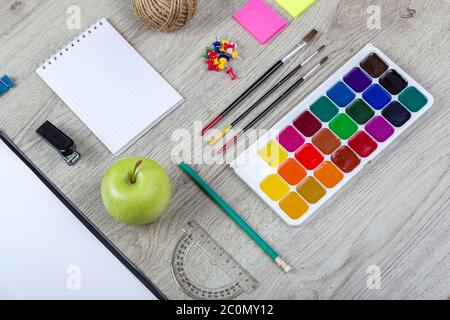 Carta, matite, pennello, mela verde su tavola di legno Foto Stock