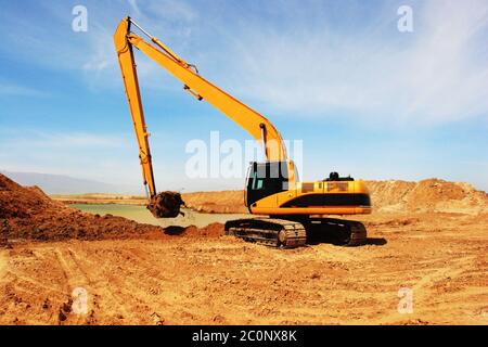 Escavatore arancione a Construction canale di irrigazione nel deserto Foto Stock