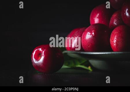 Ciliegie rosse scure su un piatto di peltro con foglie. Composizione orizzontale clooseup, scarsa illuminazione. Foto Stock