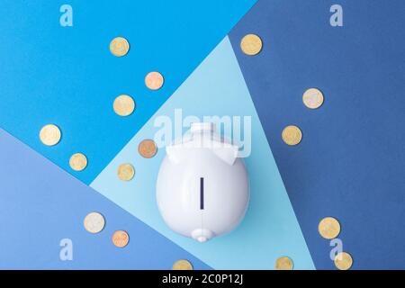 Banca bianca piggy con molte monete in euro intorno visto dall'alto con uno sfondo fresco colorato fatto da cartoncino Foto Stock