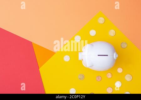 Banca bianca piggy con monete in euro intorno visto dall'alto con uno sfondo caldo colorato fatto da cartoncino Foto Stock