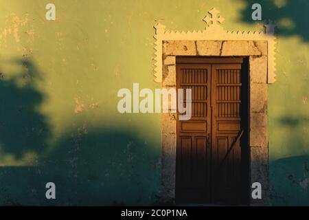 Facciata illuminata dal sole di colorata porta coloniale con cros e belle ombre a Merida, Yucatan, Messico Foto Stock