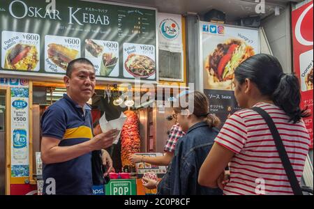 I clienti si allineano all'acquisto di cibo da uno stand kebab presso la via commerciale Ameyayokocho, Tokyo, Giappone Foto Stock