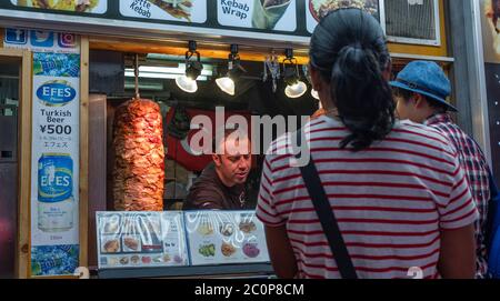 I clienti si allineano all'acquisto di cibo da uno stand kebab presso la via commerciale Ameyayokocho, Tokyo, Giappone Foto Stock