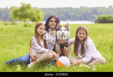 Figlia madre e cane da Husky in primo piano seduto su erba sorridente felice nel fine settimana nel parco estivo. Foto Stock