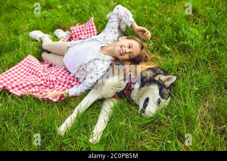 Felice bambina con bellissimo cane Husky sdraiato su coperta da picnic nel parco. Adorabile bambino che si diverte con il suo animale domestico Foto Stock