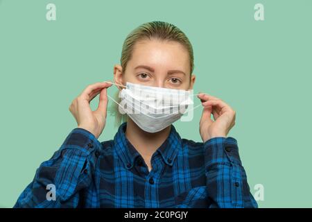 giovane donna in maschera di protezione medica guardando la fotocamera su sfondo verde Foto Stock