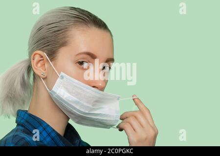 giovane donna in maschera di protezione medica guardando la fotocamera su sfondo verde Foto Stock