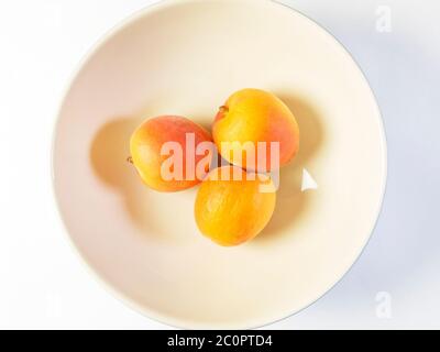 Tre albicocche fresche in una ciotola su fondo bianco Foto Stock