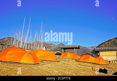 Tende arancioni nel campeggio, bandiere di preghiera sullo sfondo. Merak, Bhutan Foto Stock