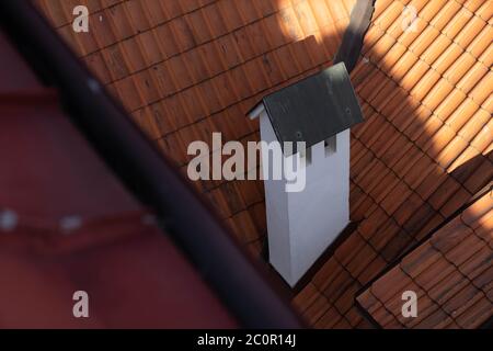 Primo piano di tubo camino bianco sul tetto in tegole rosse all'ombra. Foto Stock