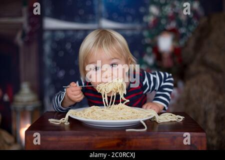 Dolce bambino, ragazzo, mangiando gli spaghetti a casa a Natale Foto Stock