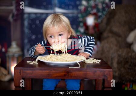 Dolce bambino, ragazzo, mangiando gli spaghetti a casa a Natale Foto Stock