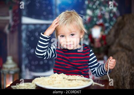 Dolce bambino, ragazzo, mangiando gli spaghetti a casa a Natale Foto Stock