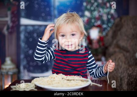 Dolce bambino, ragazzo, mangiando gli spaghetti a casa a Natale Foto Stock