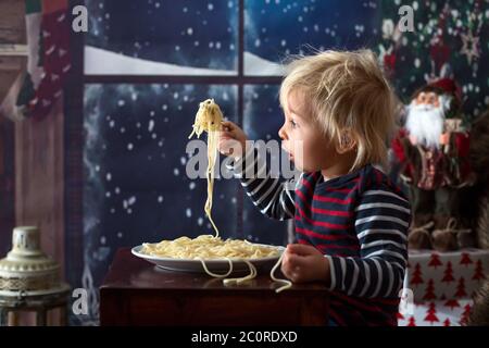 Dolce bambino, ragazzo, mangiando gli spaghetti a casa a Natale Foto Stock