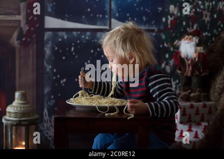 Dolce bambino, ragazzo, mangiando gli spaghetti a casa a Natale Foto Stock