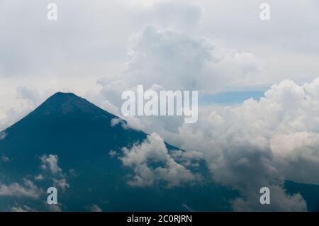 Grande cima del vulcano circondato dalla nebbia e dense nubi su campo verde Foto Stock