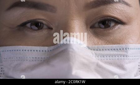 Occhi del medico di sesso femminile stanchi. Occhi di donna asiatica in maschera di sicurezza guarda la fotocamera. Primo piano Foto Stock