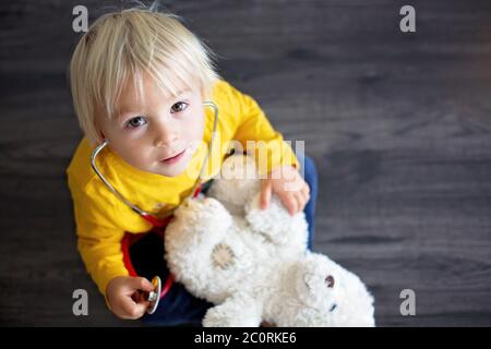 Bambino dolce, medico, che esamina il giocattolo dell'orso del bambino a casa, sfondo isolato Foto Stock