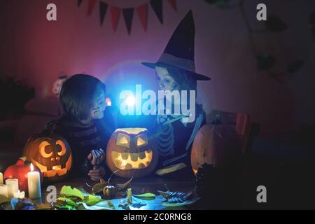 Bambini, fratelli ragazzi, giocando con zucca scolpita a casa su Halloween, facendo pozione magica Foto Stock