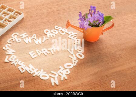 amore e salvare il concetto del mondo, alfabeto in legno forma di cuore con la parola terra all'interno e annaffiatura lattina con fiori su un tavolo di legno backgro Foto Stock