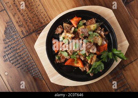 Fette di carne di agnello fritte con verdure in una padella. Sfondo di legno Foto Stock