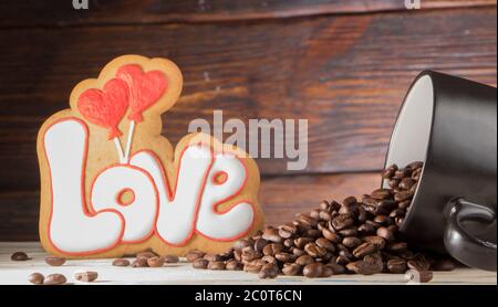 Tazza nera con semi di caffè, biscotti a forma di parola amore e due cuori rossi, su fondo di legno Foto Stock