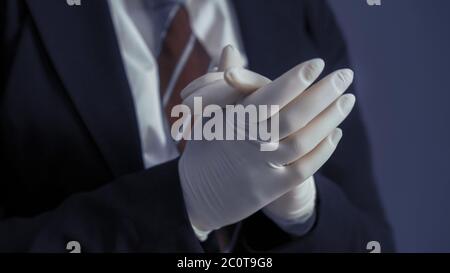 Donna d'affari in guanti di lattice protettivi e abiti da lavoro. Fuoco selettivo sulle braccia femminili che correggono i suoi guanti in primo piano. Primo piano Foto Stock