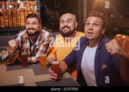 Gruppo di tifosi di calcio maschili che guardano una partita allo sport bar, bere birra. Gli uomini urlano mentre guardano la partita di calcio al pub della birra Foto Stock