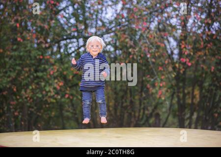 Carino bambino, ragazzo, saltando su un grande trampolino nel parco, autumntime Foto Stock