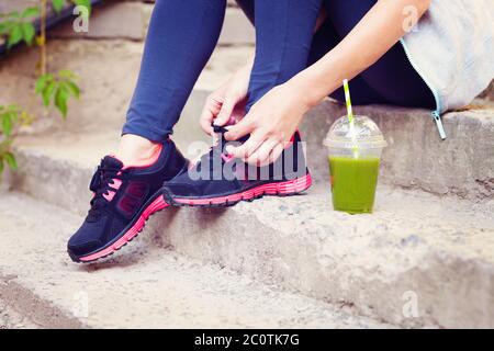 Coppa verde Detox frullato e donna allacciando scarpe da running prima dell'allenamento Foto Stock