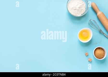 Utensili da cucina e ingredienti. Uova, farina, zucchero, frusta e spilla su fondo blu. Concetto di cottura piatto, spazio di copia. Foto Stock