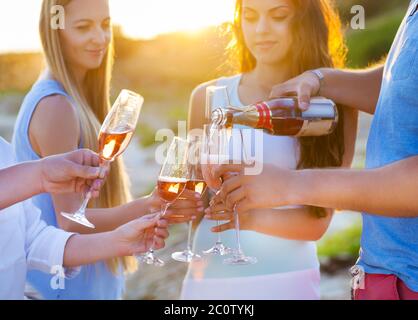 Amici felici che versano champagne in bicchieri all'aperto in spiaggia Foto Stock