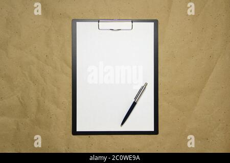 Una tavoletta con un foglio bianco di formato A4 con penna su una carta da artigianato beige. Concetto di analisi, studio, lavoro attento. Foto di scorta con spazio vuoto per il testo e il disegno. Foto Stock