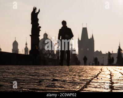La gente cammina sul ponte Carlo di mattina presto, Praga, Repubblica Ceca. Focalizzato su ciottoli. Le persone e l'architettura non sono focalizzate. Profondità di campo poco profonda. Foto Stock