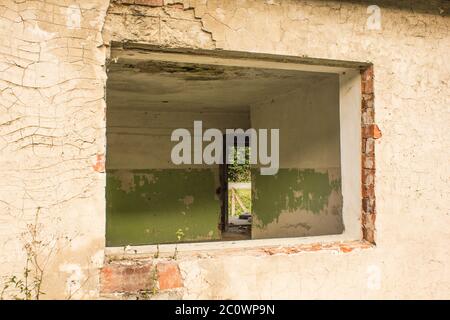 La vista dell'interno della casa abbandonata ha un telaio della finestra vuoto, la parete esterna è realizzata in cemento con notevole vernice spaccata e staccata. Foto Stock