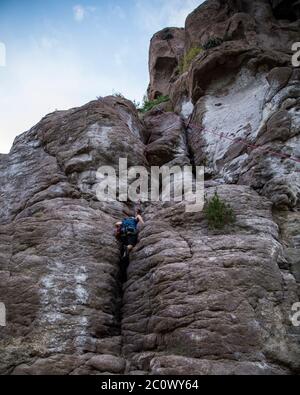 donna che sale su una montagna rocciosa, con imbracatura e casco Foto Stock