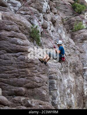 donna che sale su una montagna rocciosa, con imbracatura e casco Foto Stock