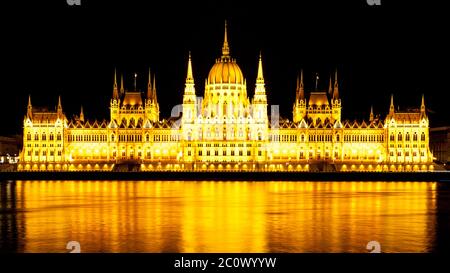 Vista panoramica notturna dell'edificio storico illuminato del Parlamento ungherese, noto anche come Orszaghaz, riflesso nell'acqua con tipica architettura simmetrica e cupola centrale sul Danubio a Budapest, Ungheria, Europa. E' un notevole punto di riferimento e sede dell'Assemblea Nazionale dell'Ungheria. Foto Stock