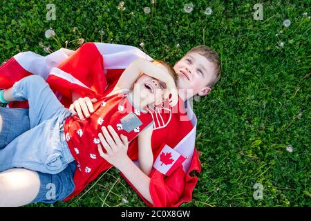 Concetto di festa della Giornata Happy Canada. Due fratelli canadesi - bambini e adolescenti all'aperto con bandiera canadese. Vista dall'alto. Foto Stock