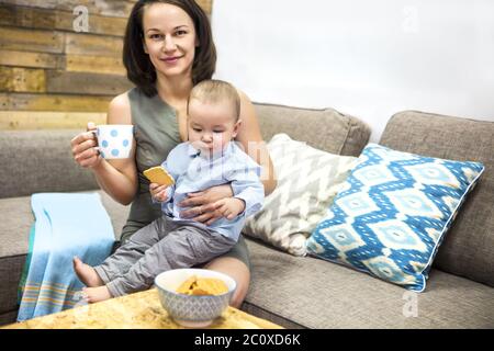 Giovane madre felice bevendo caffè e il suo bambino che mangia biscotti Foto Stock
