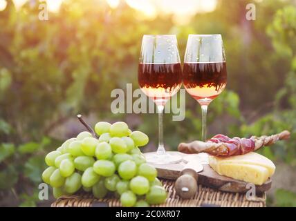 Due bicchieri di vino rosato con pane, carne, uva e formaggio Foto Stock