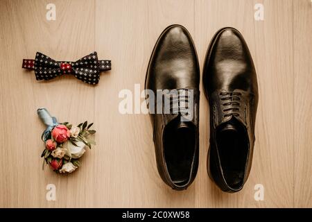 Primo piano degli accessori moderni per lo sposo. Viscere nere, scarpe in pelle e fiore boutonniere su sfondo rustico. Set per uno stile formale di indossare Foto Stock