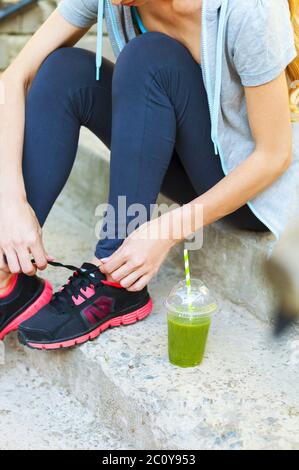 Coppa verde Detox frullato e donna allacciando scarpe da running prima dell'allenamento Foto Stock