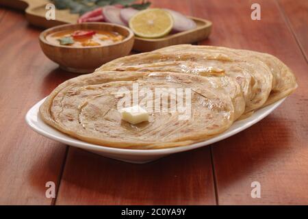 Kerala Parotta/porotta/paratha/pane piatto a strati fatto in casa utilizzando il grano popolare nel sud dell'India, servito in una tavola di legno con sfondo di legno marrone Foto Stock