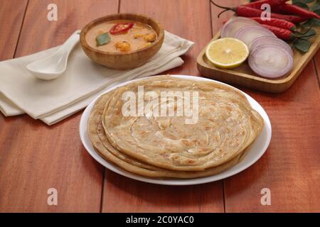 Kerala Parotta/porotta/paratha/pane piatto a strati fatto in casa utilizzando il grano popolare nel sud dell'India, servito in una tavola di legno con sfondo di legno marrone Foto Stock