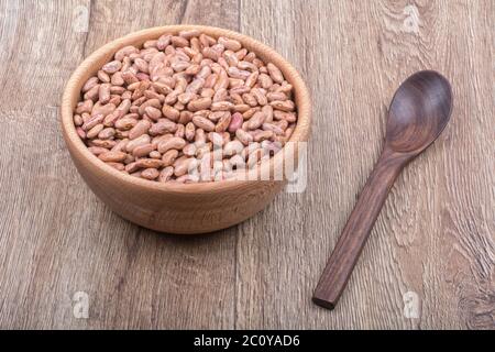 Ciotola con fagioli e cucchiaio di legno su fondo di legno Foto Stock